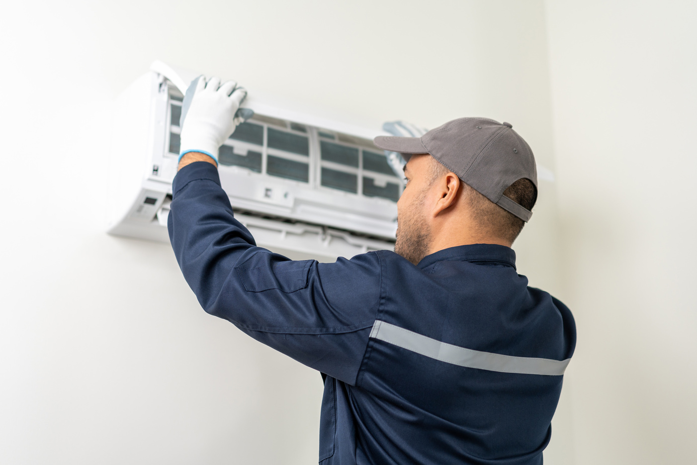 Air conditioner service indoors. Air conditioner cleaning technician He opened the front cover and took out the filters and washed it. He in uniform wearing rubber